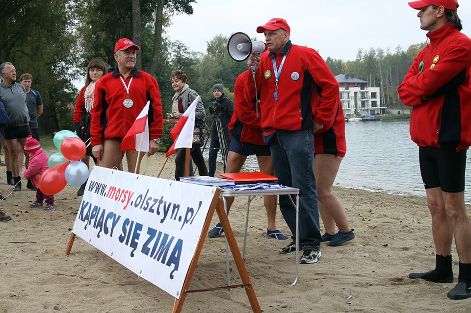 Morsy z Olsztyna podczas inauguracji sezonu zimowego na plaży nad jeziorem, wśród uczestników i organizatorów.