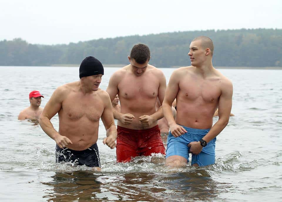 Mężczyźni w kąpieli zimowej na plaży, trzymają się za ręce i wchodzą do wody.