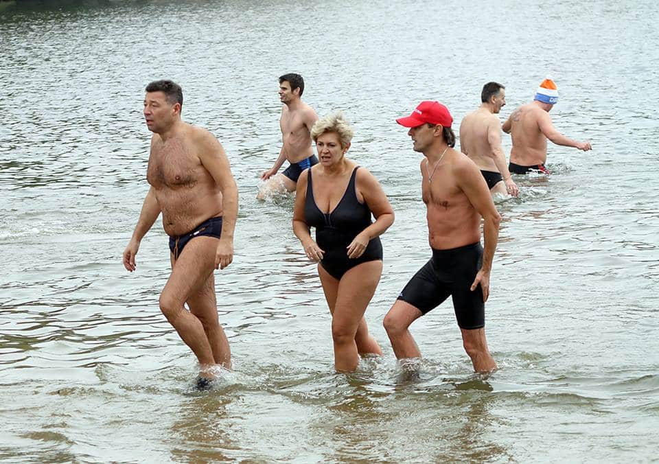 Grupa ludzi kąpie się w zimnym jeziorze podczas inauguracji sezonu zimowych kąpieli.