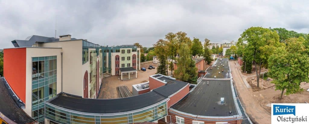 Widok na nowe obiekty szpitala z góry, w otoczeniu drzew i placu budowy.