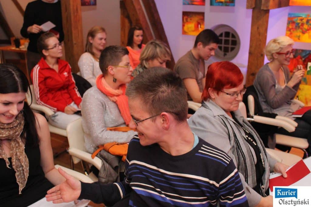 Grupa ludzi siedzących w sali podczas finału slamu poetyckiego, większość z nich patrzy na scenę, uśmiechając się i rozmawiając.