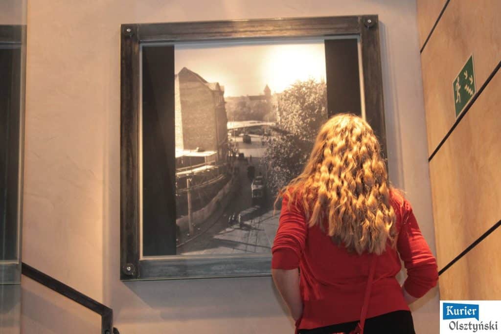 Kobieta z długimi, kręconymi włosami ogląda czarno-białą fotografię na wystawie w galerii.