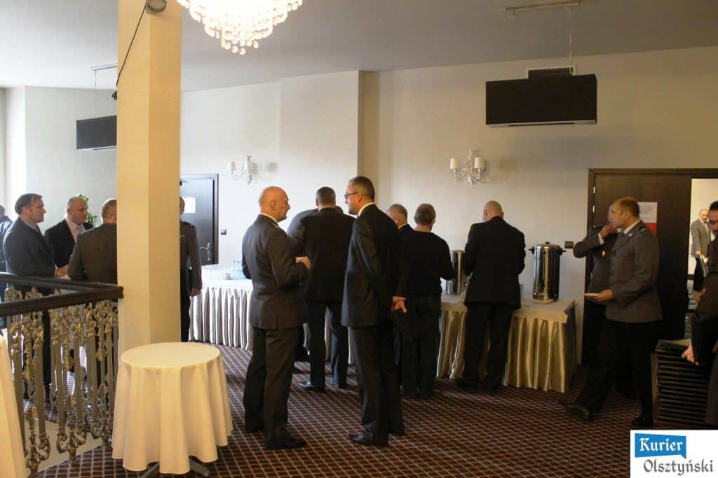 Grupa osób w eleganckich strojach podczas spotkania w sali konferencyjnej, przy bufecie z kawą.