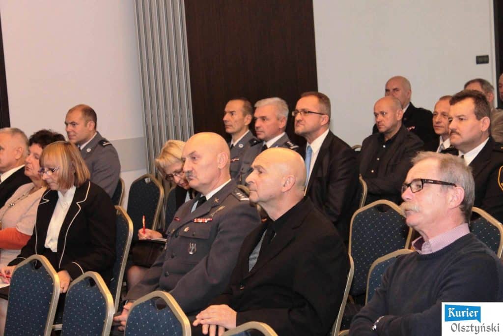 Uczestnicy konferencji w sali podczas słuchania prelekcji, w tym mężczyźni w mundurach i cywile.