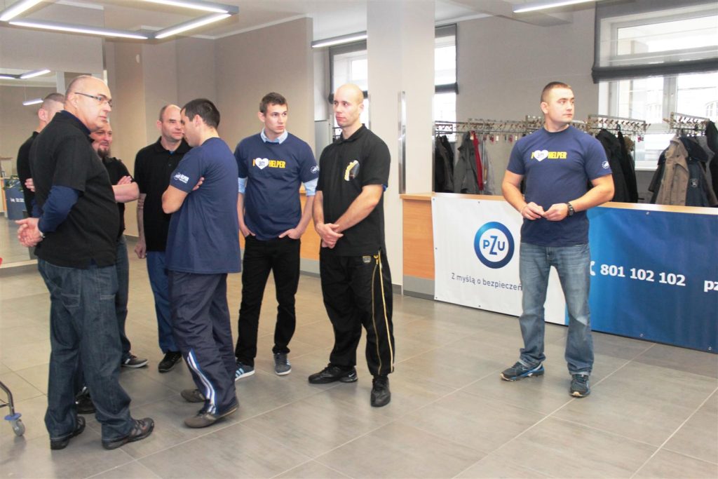 Grupa osób rozmawia podczas gali w urzędzie, w tle widoczne są plakaty i ubrania na stojakach.