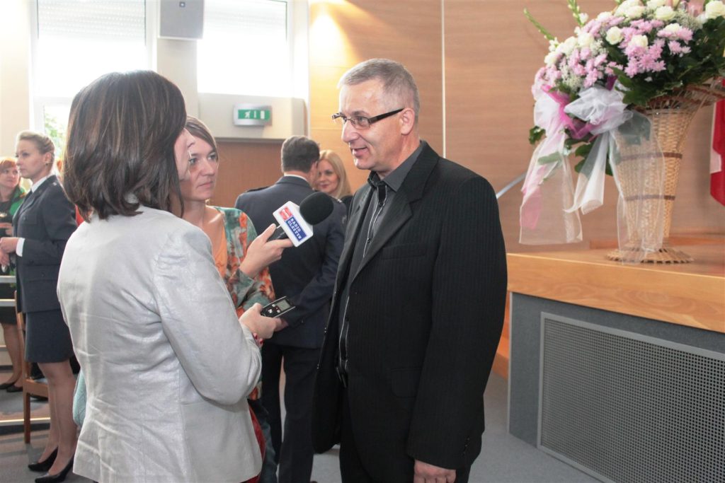Mężczyzna mówi w wywiadzie do dziennikarki podczas gali finałowej w urzędzie wojewódzkim, w tle dekoracje i inni uczestnicy.
