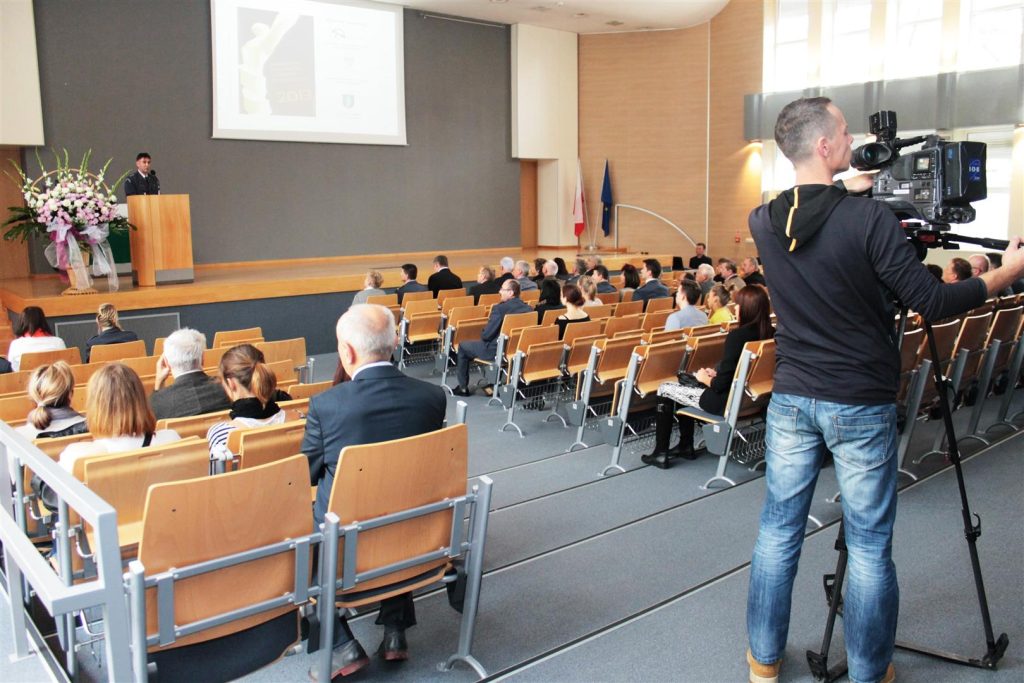 Sala konferencyjna z uczestnikami gali i kamerzystą filmującym wydarzenie.