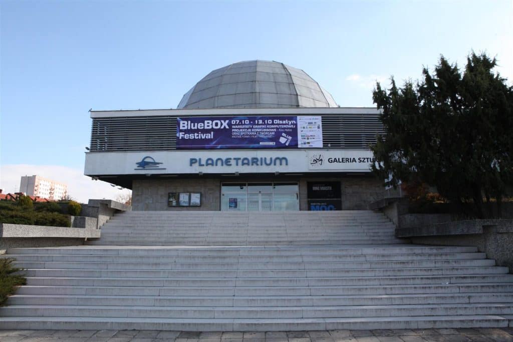 Widok na planetarium z dużym banerem festiwalu BlueBox przed wejściem, widoczne schody i drzwi.