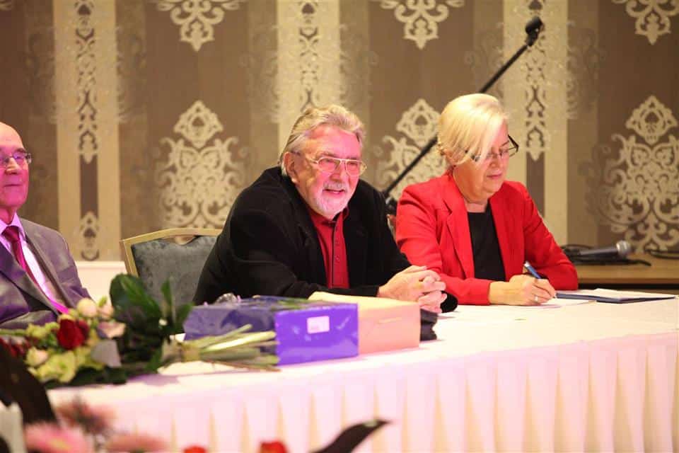 Uroczystość jubileuszowa Akademii Trzeciego Wieku w sali konferencyjnej, z uczestnikami i gośćmi przy stole.
