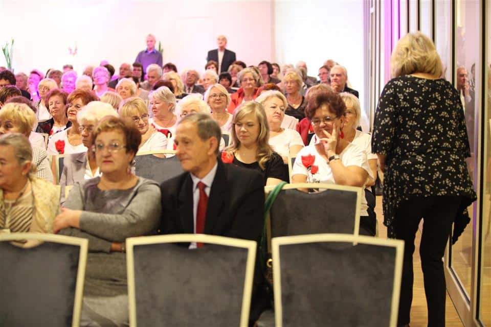 Uczestnicy wydarzenia Akademii Trzeciego Wieku podczas uroczystości jubileuszowej w sali konferencyjnej, z przewagą seniorów, w tle widoczny prezydent.