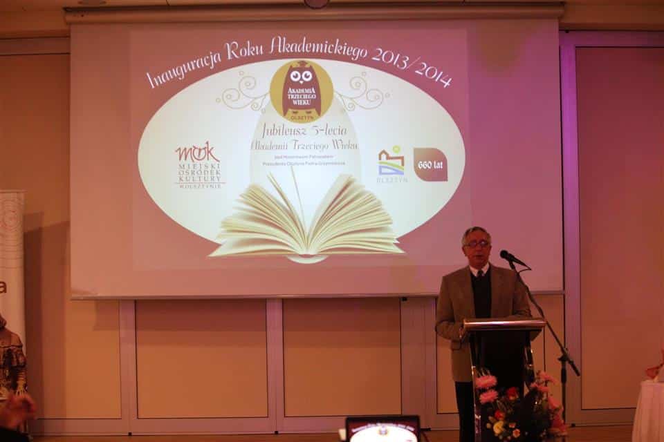 Mężczyzna przemawia z podium podczas jubileuszowej inauguracji Akademii Trzeciego Wieku w Olsztynie.