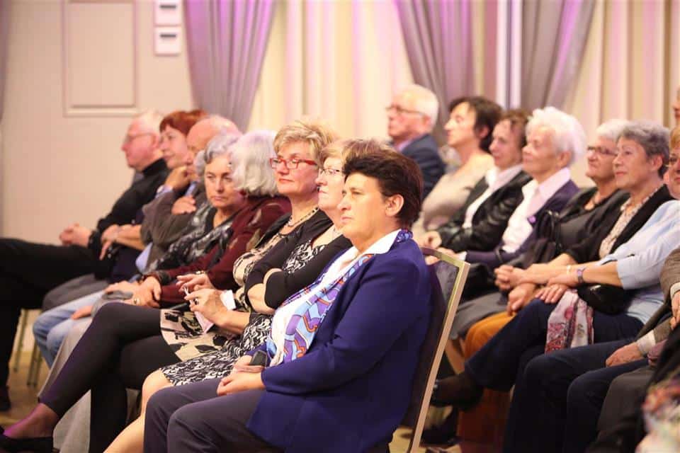 Grupa starszych osób siedzi w sali podczas uroczystości jubileuszowej Akademii Trzeciego Wieku.