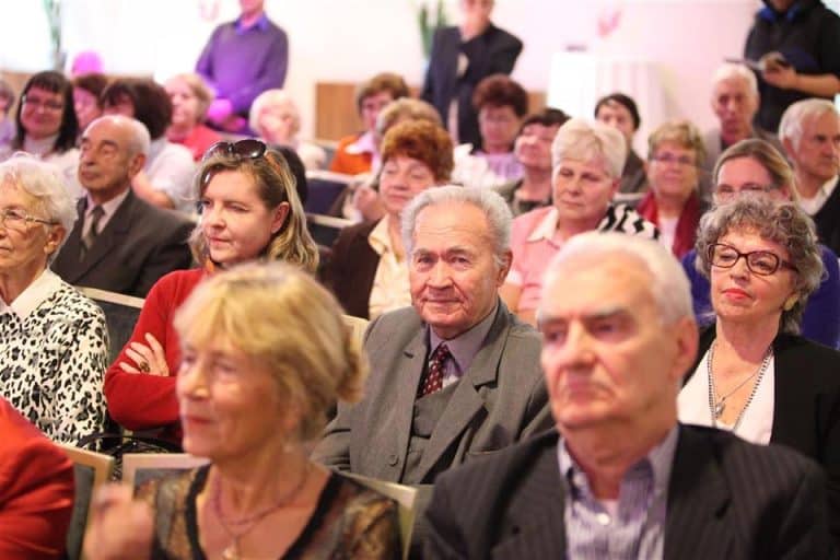 Uczestnicy ceremonii jubileuszowej Akademii Trzeciego Wieku w Sali konferencyjnej, na zdjęciu widoczna grupa starszych osób siedząca podczas wydarzenia.