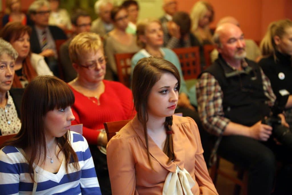 Widownia podczas wydarzenia kulturalnego w Kamienicy Naujackiej, z osobami słuchającymi dyskusji.