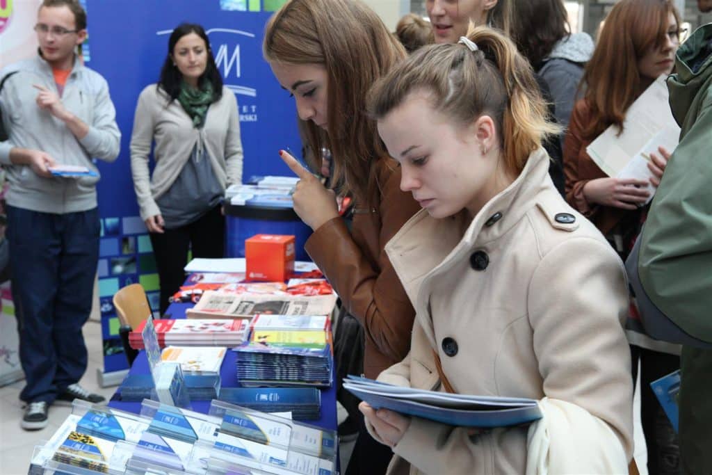 Grupa młodych ludzi przegląda materiały promocyjne podczas targów pracy w Centrum Konferencyjno-Szkoleniowym UWM.