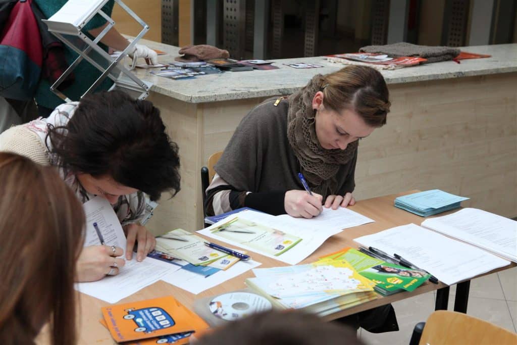 Kobiety siedzą przy stoliku, wypełniają dokumenty podczas targów pracy w Kortowie.