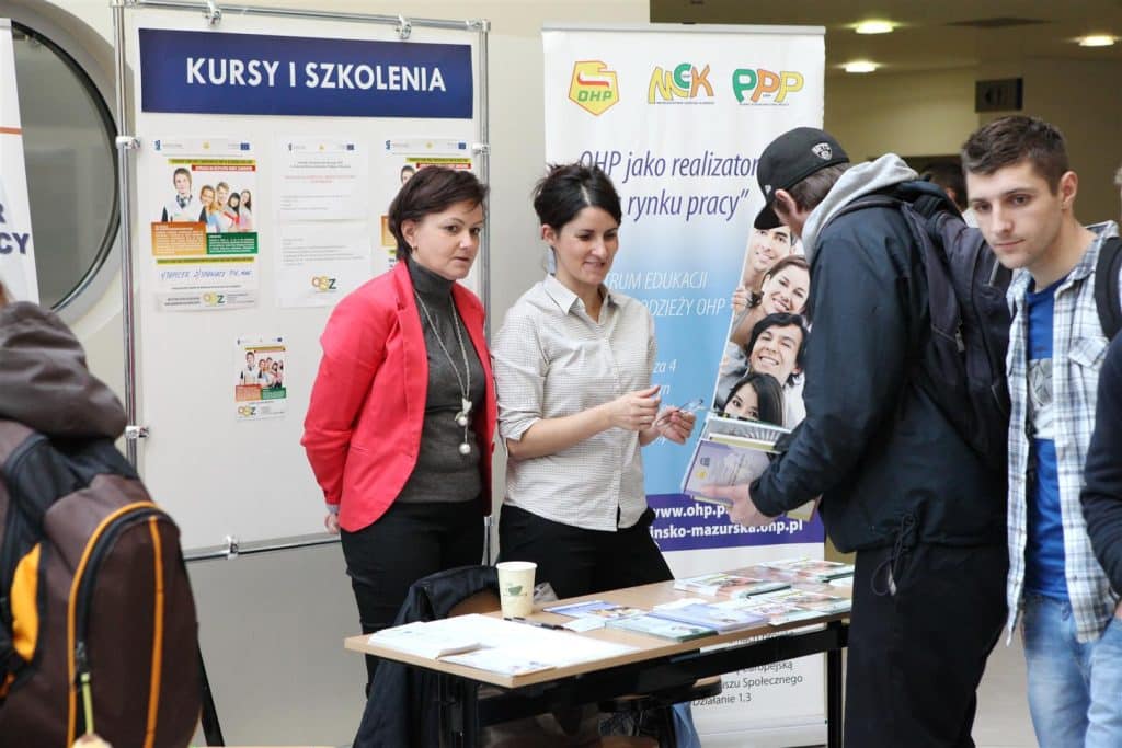 Uczestnicy rozmawiają przy stoisku z ofertami edukacyjnymi i szkoleniowymi podczas targów w Kortowie.