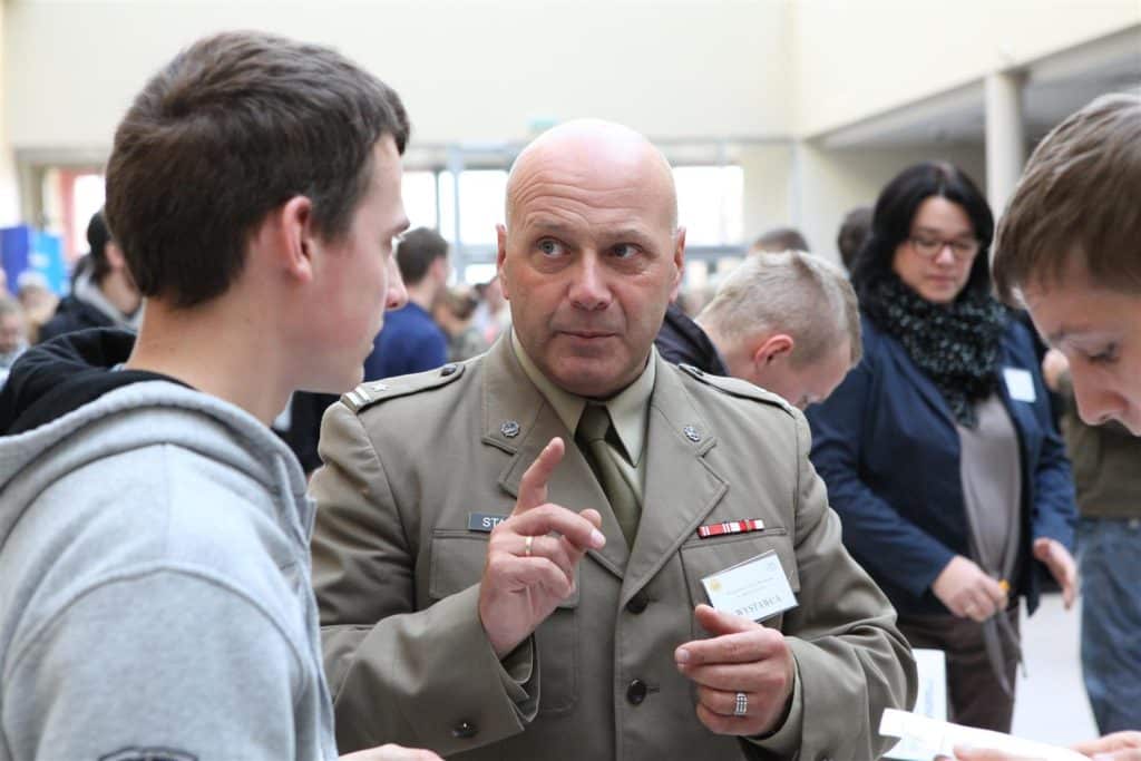 Mężczyzna w wojskowym mundurze rozmawia z młodym uczestnikiem targów