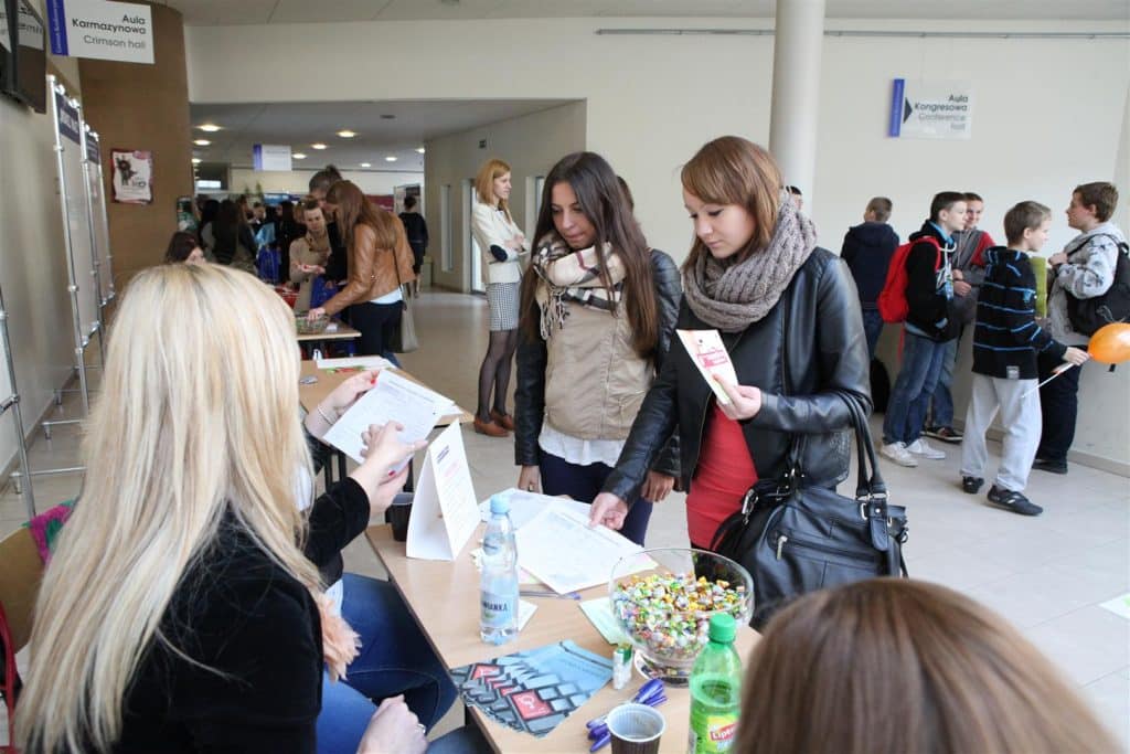 Młodzież podczas targów pracy w Centrum Konferencyjno-Szkoleniowym UWM, rozmawiająca i przeglądająca materiały informacyjne.