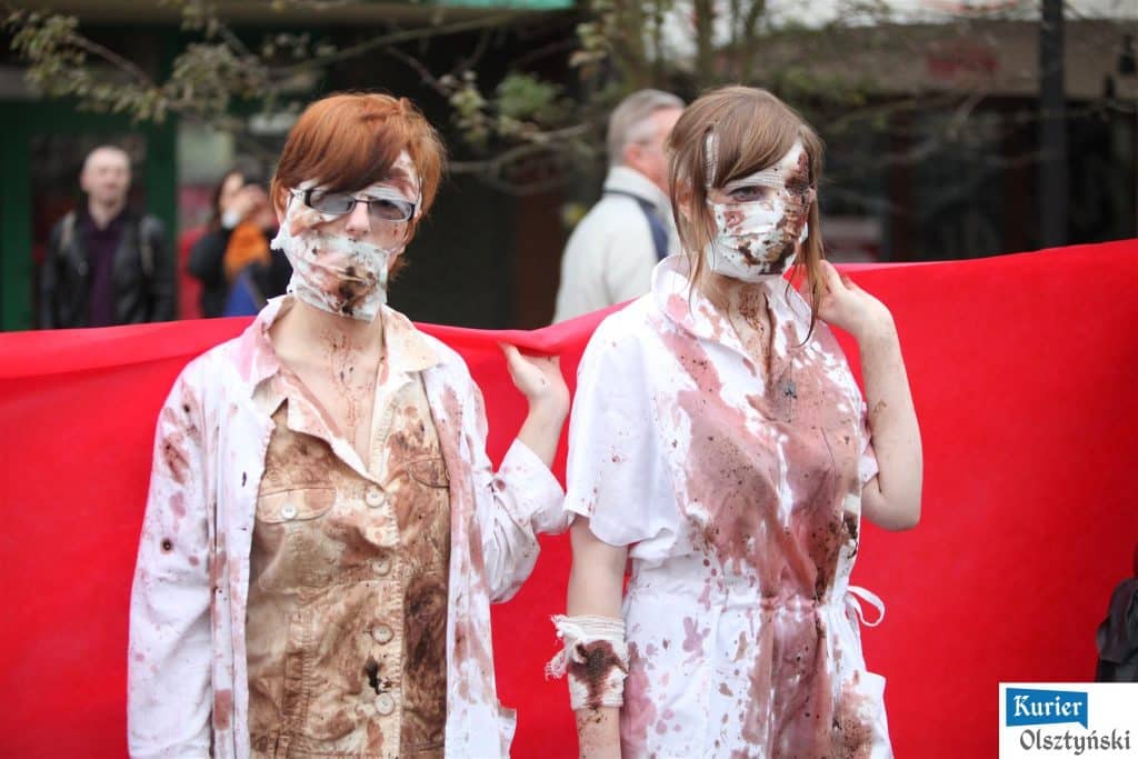 Dwie dziewczyny w przebraniu zombie na tle czerwonego materiału podczas obchodu jubileuszu szkoły plastycznej.