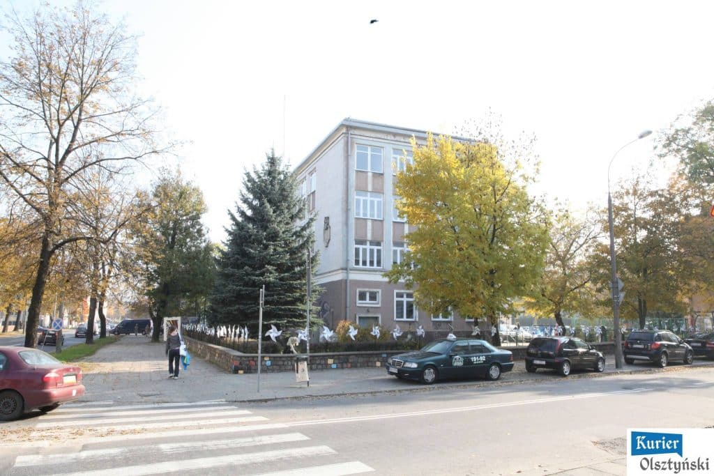 Widok na budynek Państwowego Liceum Plastycznego w Olsztynie z drzewami w jesiennej kolorystyce.