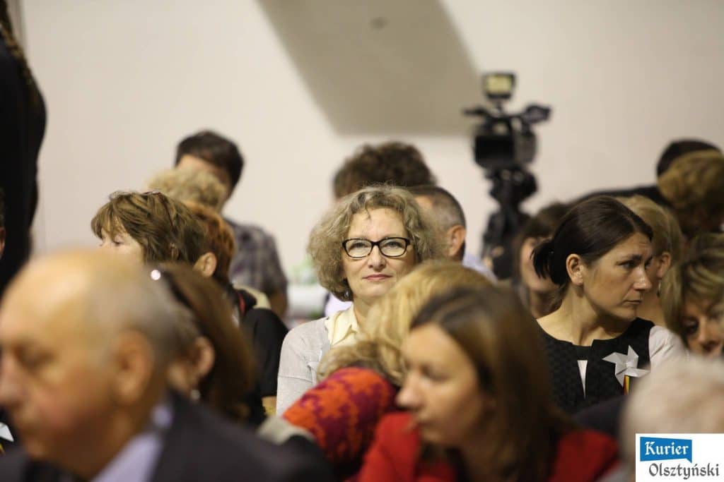 Grupa osób na uroczystości 25-lecia szkoły plastycznej, w tle kamera nagrywająca wydarzenie.