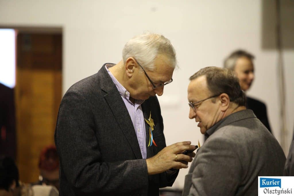 Dwa mężczyźni rozmawiają i wymieniają się medalami podczas uroczystości.