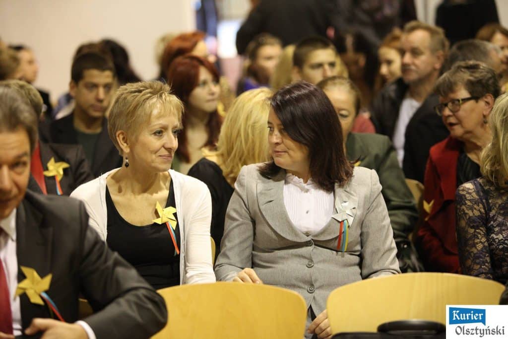 Grupa osób siedzi na sali podczas uroczystości z okazji 25-lecia szkoły plastycznej, rozmawiają i uważnie słuchają.