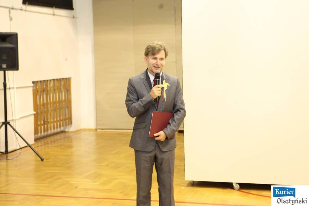 Mężczyzna w garniturze mówi do mikrofonu podczas uroczystości w szkole plastycznej.