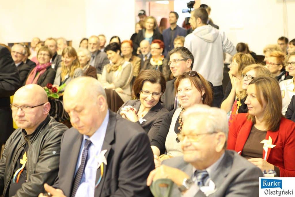 Uczestnicy uroczystości 25-lecia szkoły artystycznej, siedzą i śmieją się podczas wydarzenia.