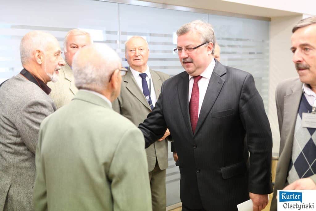 Grupa mężczyzn rozmawia i wita się podczas otwarcia wystawy w Urzędzie Wojewódzkim.