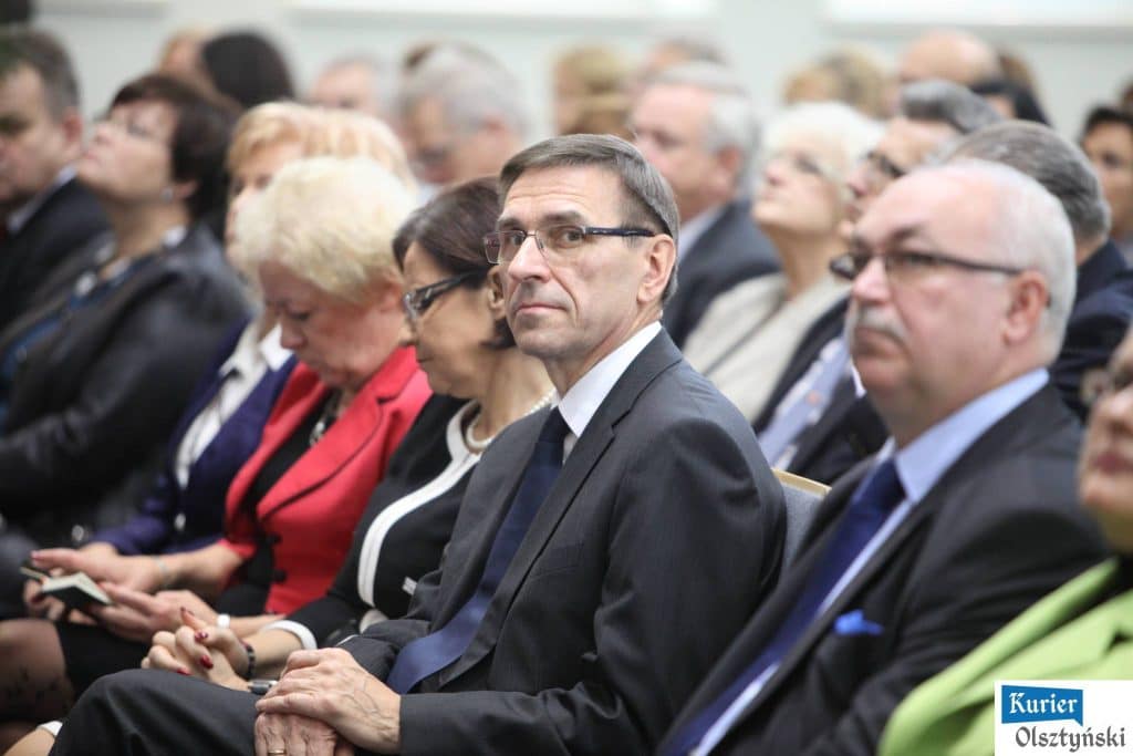 Uczestnicy uroczystości Dnia Edukacji Narodowej siedzą w sali, wśród nich mężczyźni w garniturach i kobiety w eleganckich strojach.