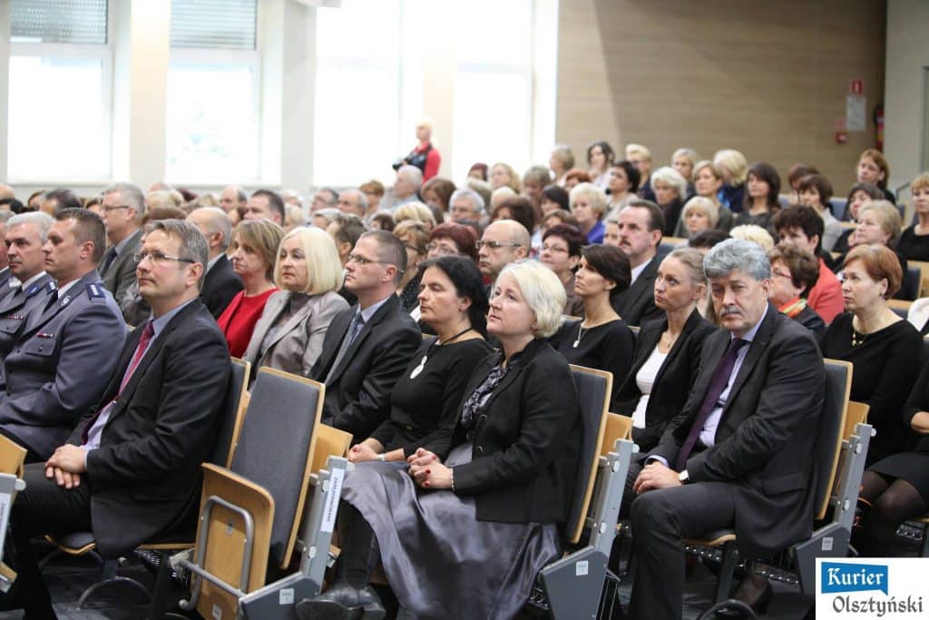 Uczestnicy uroczystości Dnia Edukacji Narodowej siedzą w auli, słuchając prelekcji, wśród nich policjanci i nauczyciele.