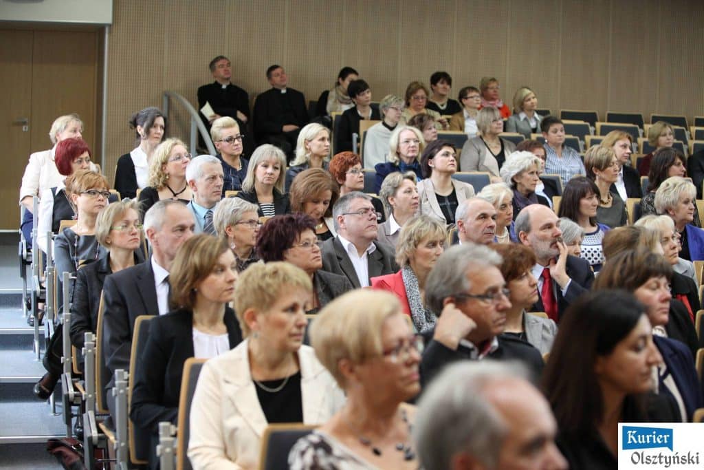 Uczestnicy oficjalnych obchodów Dnia Edukacji Narodowej w sali konferencyjnej, z przodu kobiety i mężczyźni w formalnych strojach.