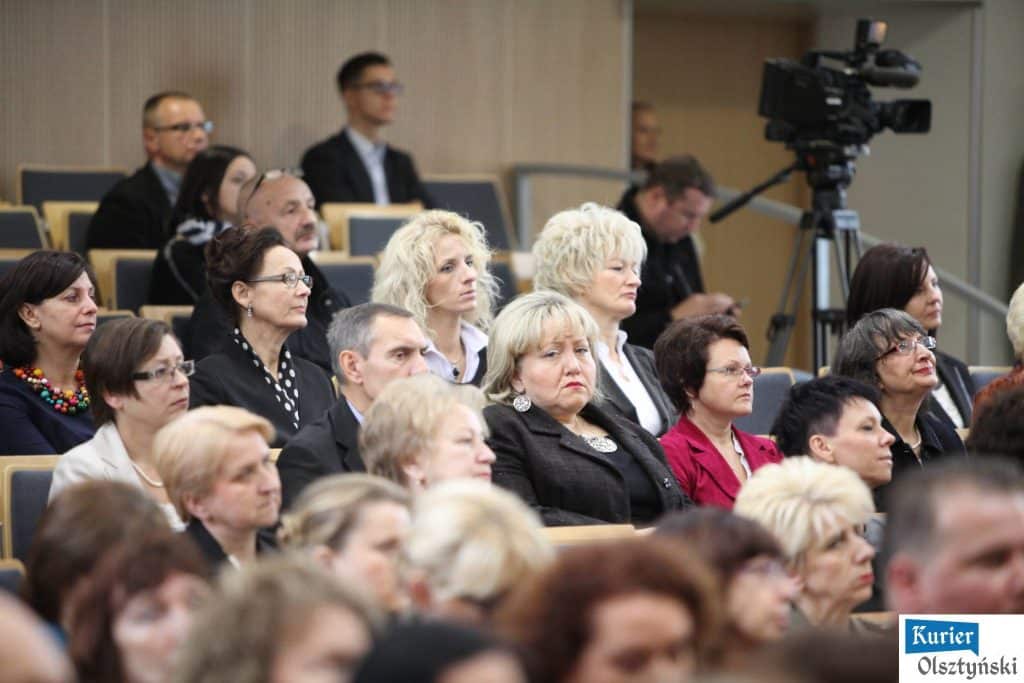 Uczestnicy uroczystości Dnia Edukacji Narodowej podczas gali w Urzędzie Wojewódzkim, na pierwszym planie kobiety z wyrazistymi fryzurami i dodatkami.