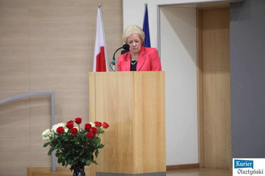 Kobieta w czerwonym żakiecie przemawia z podium podczas oficjalnych obchodów Dnia Edukacji Narodowej.