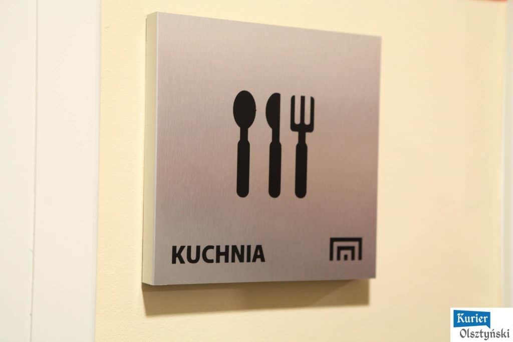 Tabliczka z ikonami sztućców i napisem "Kuchnia" na ścianie budynku teatru.