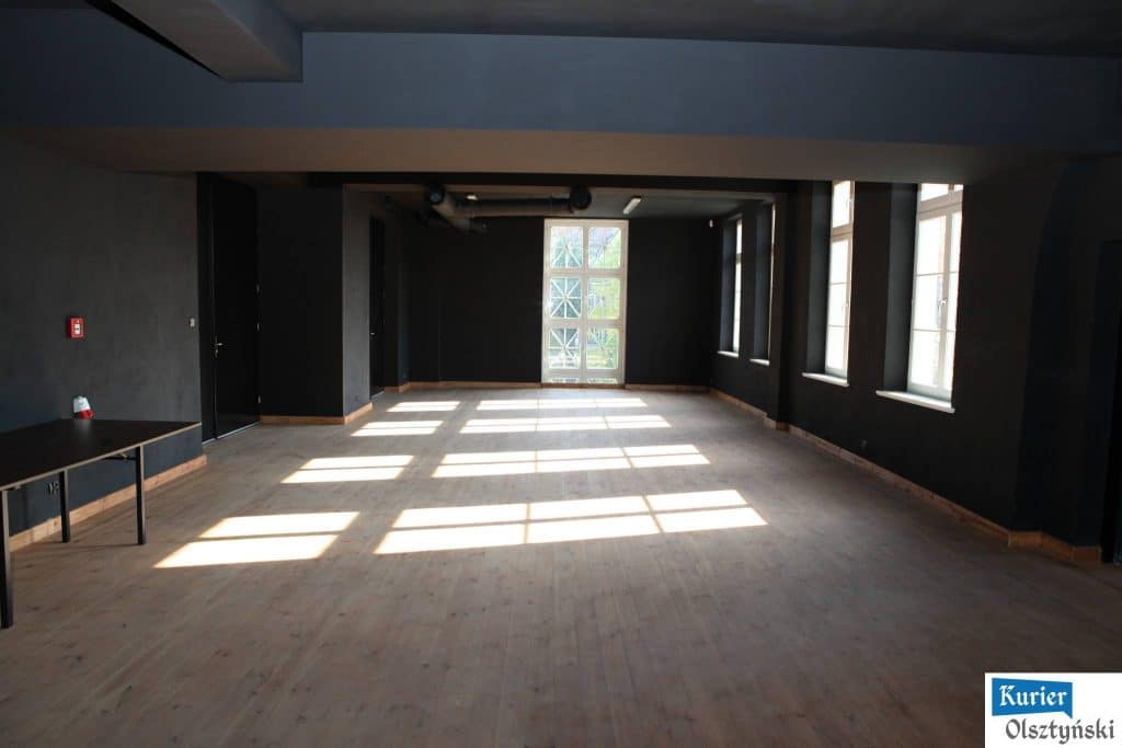 Puste sala w nowoczesnym teatrze z dużymi oknami i naturalnym oświetleniem.