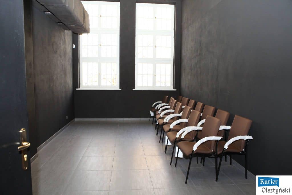 Pusta sala teatralna w nowoczesnym stylu z czarnymi ścianami, dużymi oknami i rzędami foteli.