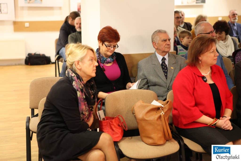 Osoby siedzące na publiczności podczas ceremonii wręczenia nagród w Olsztynie, widoczne głównie kobiety i starszy mężczyzna.