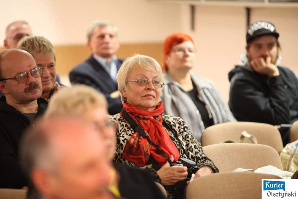 Zgromadzeni ludzie podczas ceremonii wręczenia nagród w Planetarium, na pierwszym planie starsza kobieta z blond włosami, okularami i czerwonym szalikiem.