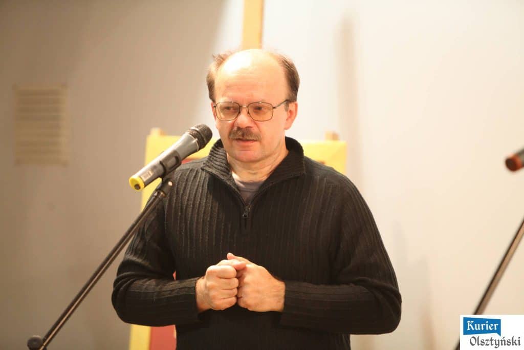 Mężczyzna w czarnym swetrze mówi do mikrofonu podczas ceremonii wręczenia nagród.