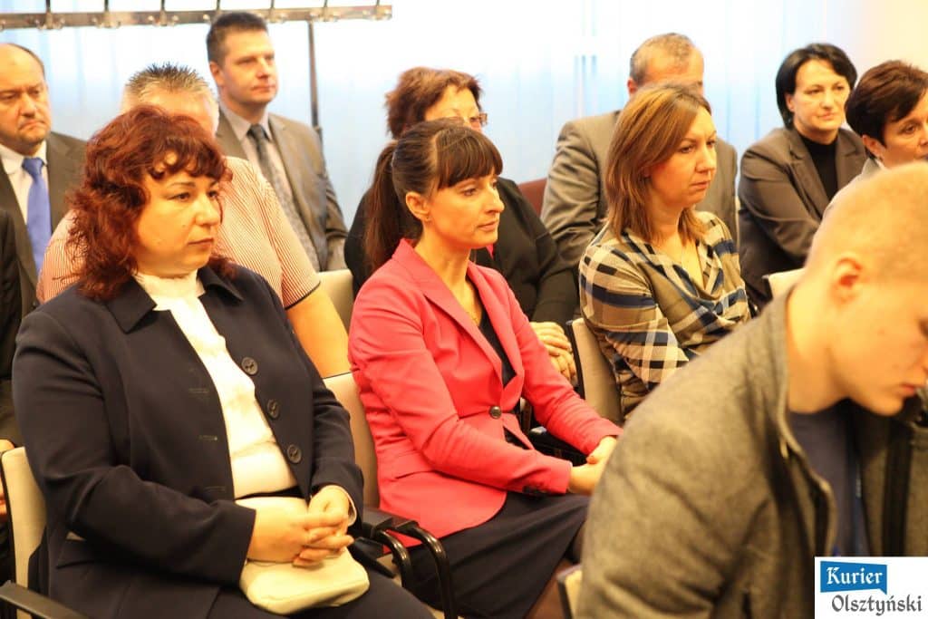 Zdjęcie przedstawia grupę dorosłych osób siedzących na sali podczas oficjalnego wydarzenia, prawdopodobnie konferencji lub ceremonii.