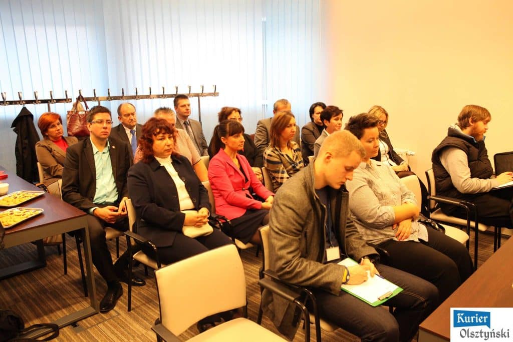 Grupa ludzi siedzi na sali podczas konferencji przed zawodami pływackimi w Aquasferze.