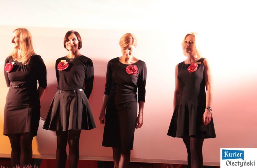 Magda Umer na scenie podczas inauguracji BabaFest, ubrana w czarną sukienkę z czerwonym kwiatem na piersi.