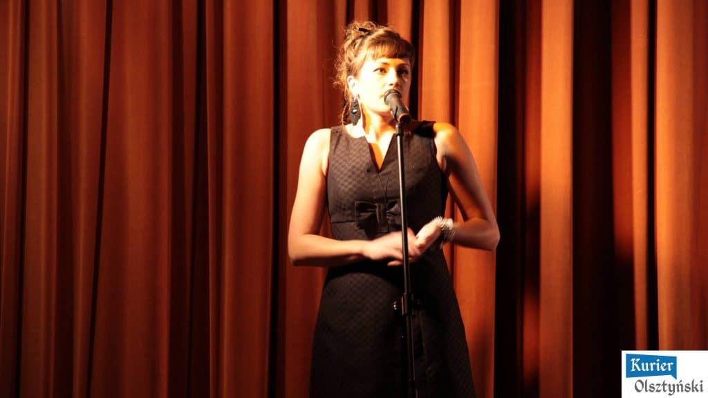 Magda Umer na scenie podczas inauguracji BabaFest w Auditorium Maximum, w otoczeniu pomarańczowych zasłon.