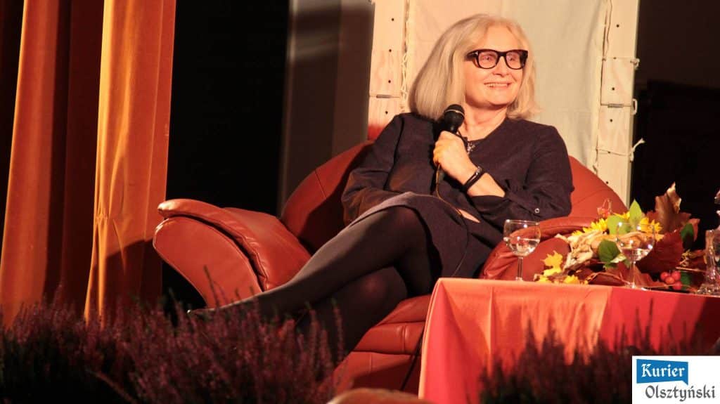 Magda Umer siedzi na kanapie, trzyma mikrofon, uśmiecha się podczas wydarzenia.