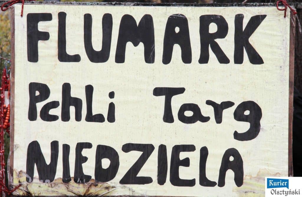 Tablica z napisem o sprzedaży na pchlim targu, ręcznie malowana, na tle innych straganów.