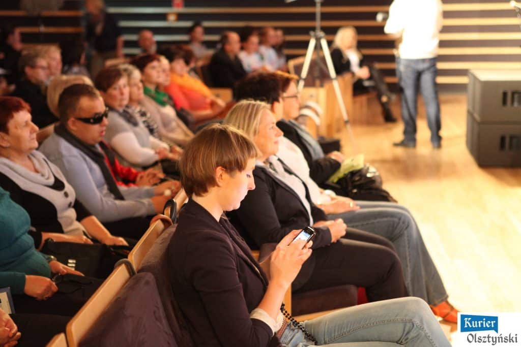 Kobiety podczas kongresu w filharmonii w Olsztynie, słuchają prelegentów i korzystają z telefonów.