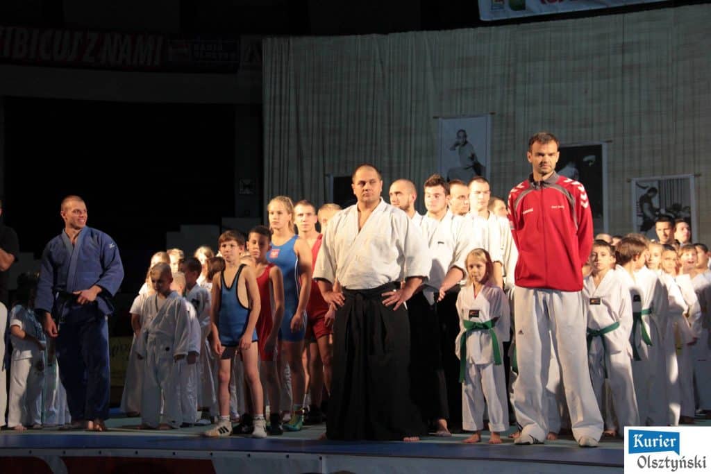 Grupa sportowców i dzieci na scenie podczas festiwalu sztuk walki w hali Urania.